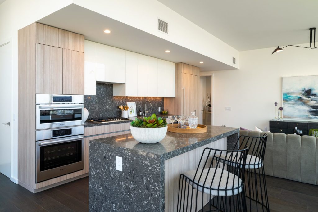 Two Bedroom Residences in Downtown Los Angeles, CA - THEA at Metropolis - Kitchen with Grey Countertops and Backsplash, Island with Bar Chairs, and Appliances